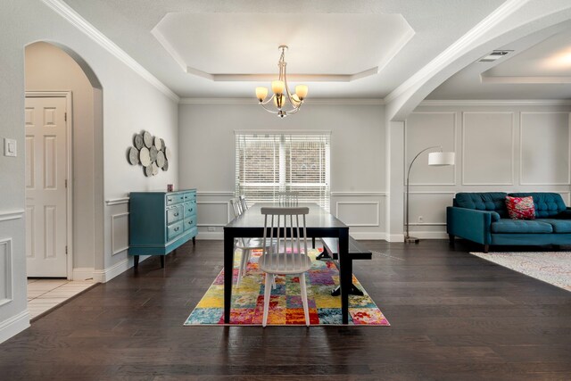 dining room with arched walkways, a notable chandelier, a raised ceiling, a decorative wall, and wood finished floors