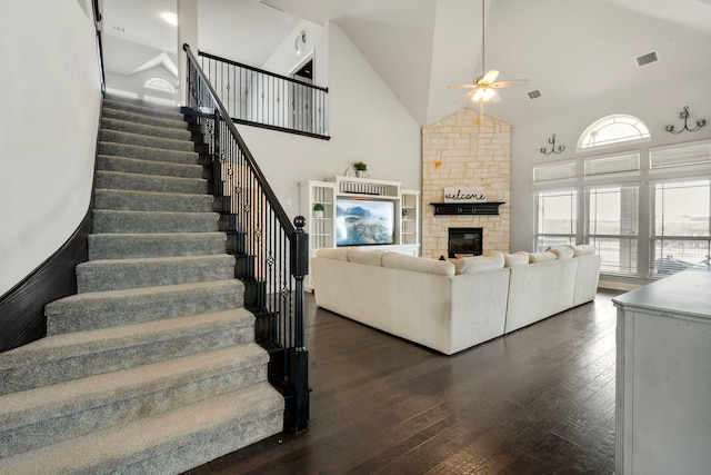 living area with a stone fireplace, dark wood-type flooring, high vaulted ceiling, and visible vents