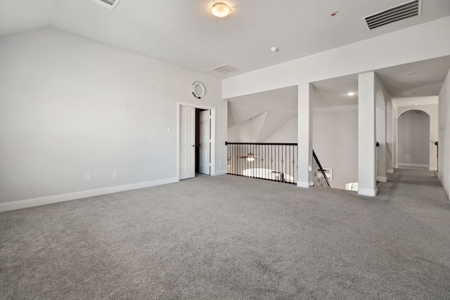 carpeted empty room with arched walkways, lofted ceiling, visible vents, and baseboards