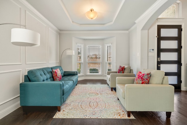 living area featuring arched walkways, a raised ceiling, a decorative wall, dark wood-type flooring, and ornamental molding