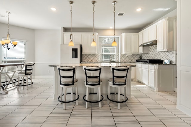 kitchen featuring under cabinet range hood, a breakfast bar, visible vents, tasteful backsplash, and smart refrigerator