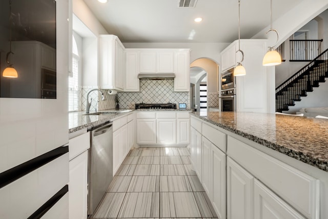 kitchen with stone counters, decorative backsplash, appliances with stainless steel finishes, a sink, and under cabinet range hood