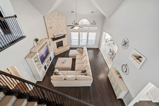 living area featuring arched walkways, a fireplace, wood finished floors, high vaulted ceiling, and stairs