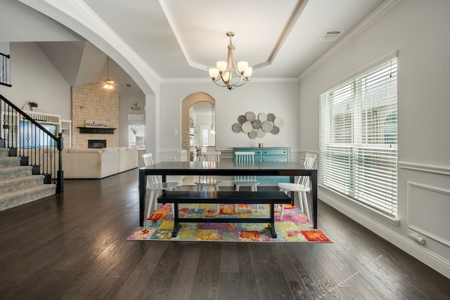 dining area with a tray ceiling, hardwood / wood-style flooring, wainscoting, a stone fireplace, and stairs
