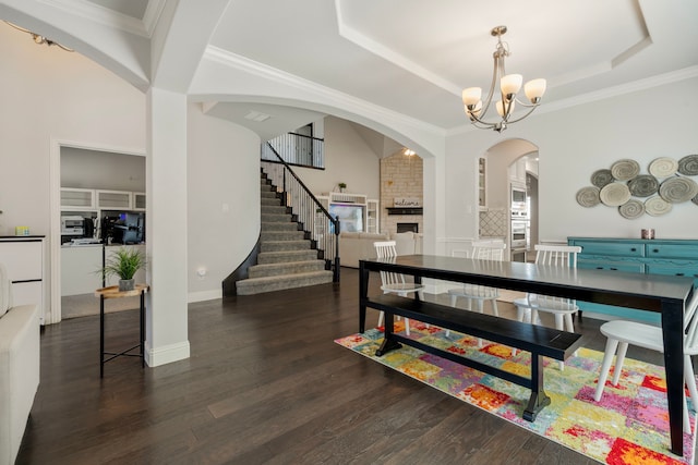 dining space with a raised ceiling, stairway, dark wood-type flooring, a large fireplace, and a chandelier