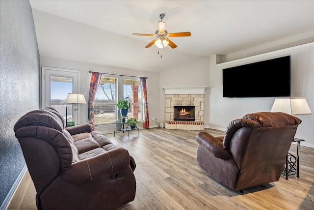 living room with vaulted ceiling, a stone fireplace, baseboards, and wood finished floors