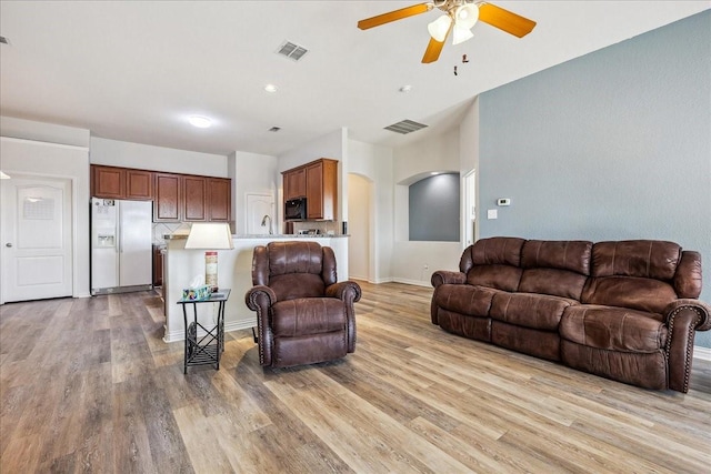 living area with visible vents, arched walkways, light wood-style floors, and a ceiling fan