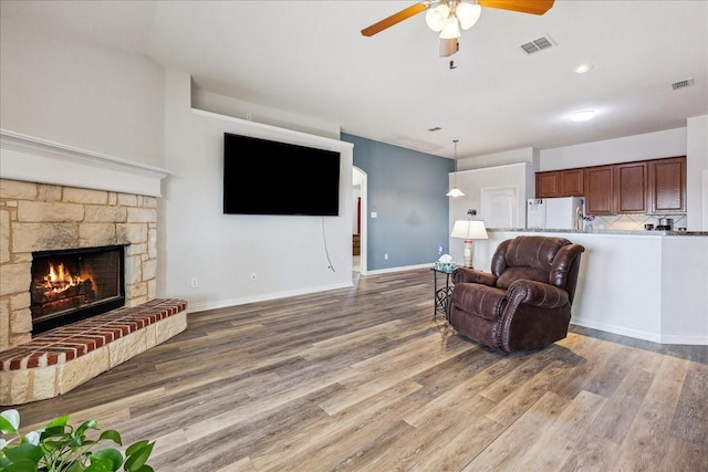 living area with visible vents, a stone fireplace, baseboards, and wood finished floors