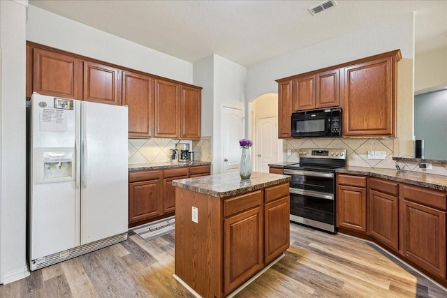 kitchen featuring visible vents, black microwave, double oven range, light wood-style floors, and white fridge with ice dispenser