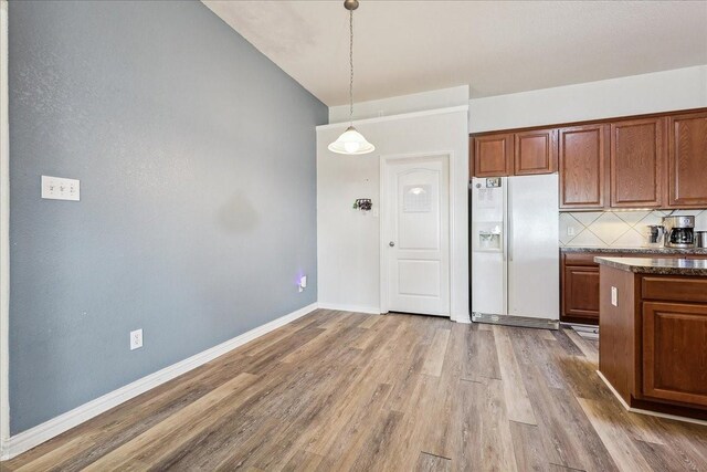 kitchen with backsplash, baseboards, white refrigerator with ice dispenser, wood finished floors, and hanging light fixtures