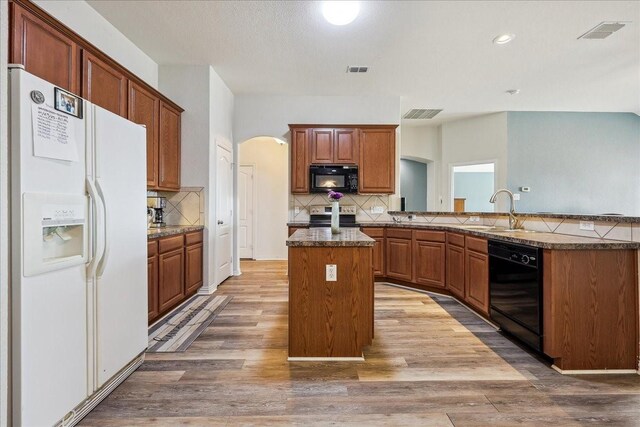 kitchen featuring a kitchen island, wood finished floors, arched walkways, black appliances, and a sink