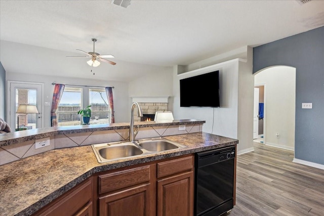 kitchen with open floor plan, black dishwasher, a stone fireplace, arched walkways, and a sink