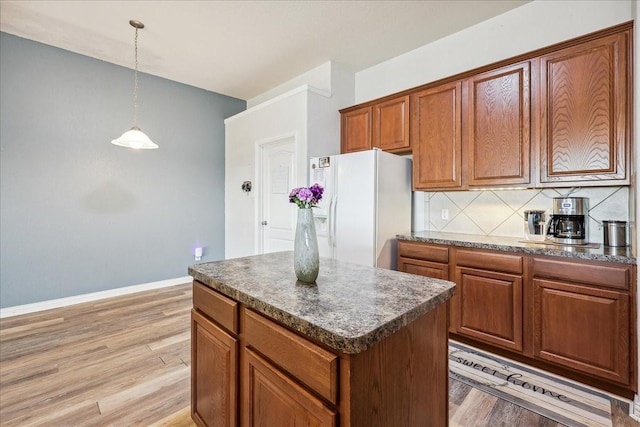 kitchen featuring dark countertops, tasteful backsplash, brown cabinets, white refrigerator with ice dispenser, and light wood-style floors