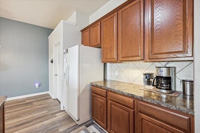 kitchen with brown cabinetry, light wood-style flooring, decorative backsplash, white fridge with ice dispenser, and dark countertops