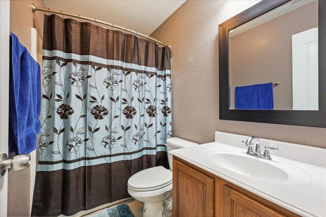 bathroom with vanity, a shower with curtain, toilet, and a textured wall