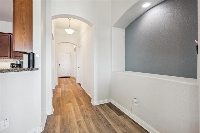 hall featuring arched walkways, light wood-style flooring, and baseboards