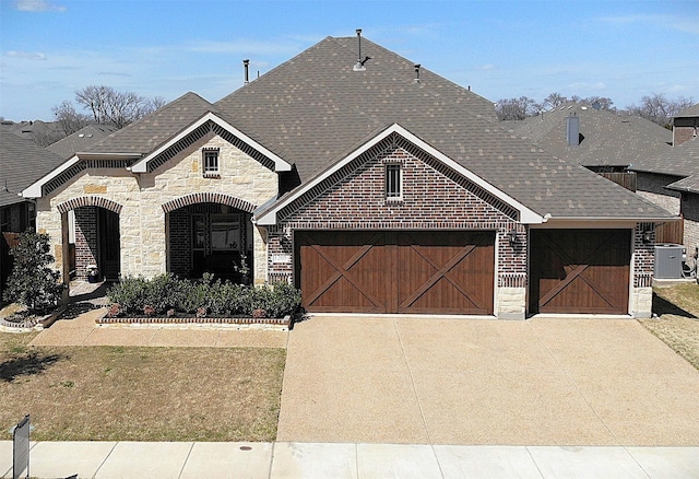 french country style house featuring a garage, central air condition unit, roof with shingles, and stone siding