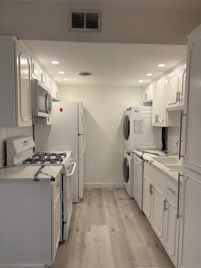 kitchen with stacked washer and dryer, white range with gas cooktop, light wood finished floors, visible vents, and stainless steel microwave