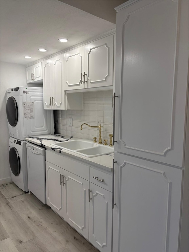 kitchen featuring light wood finished floors, tasteful backsplash, stacked washer / dryer, a sink, and white appliances