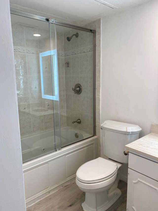 bathroom featuring toilet, combined bath / shower with glass door, wood finished floors, and vanity