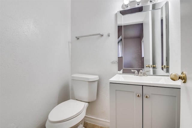 half bathroom featuring baseboards, toilet, vanity, and a textured wall