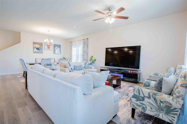 living area featuring ceiling fan with notable chandelier, wood finished floors, visible vents, and baseboards