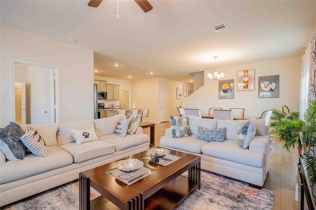 living area featuring light wood-type flooring, ceiling fan with notable chandelier, visible vents, and recessed lighting