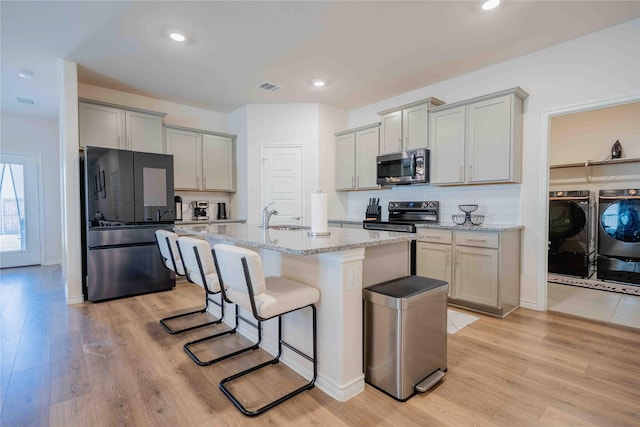 kitchen with appliances with stainless steel finishes, light wood-type flooring, washing machine and dryer, and a breakfast bar