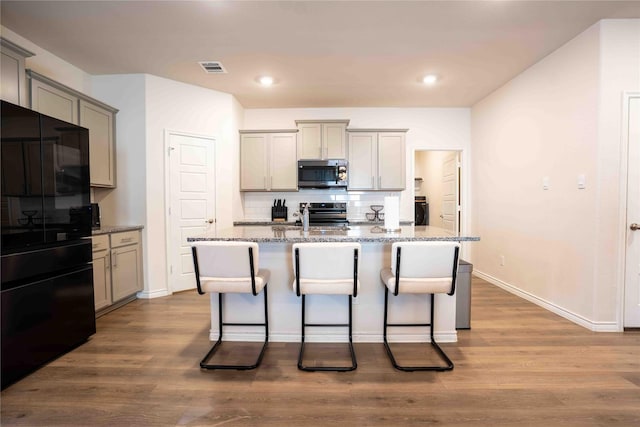 kitchen with appliances with stainless steel finishes, stone countertops, gray cabinets, and wood finished floors