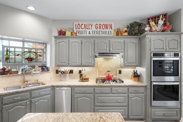 kitchen featuring under cabinet range hood, stainless steel appliances, a sink, gray cabinets, and backsplash