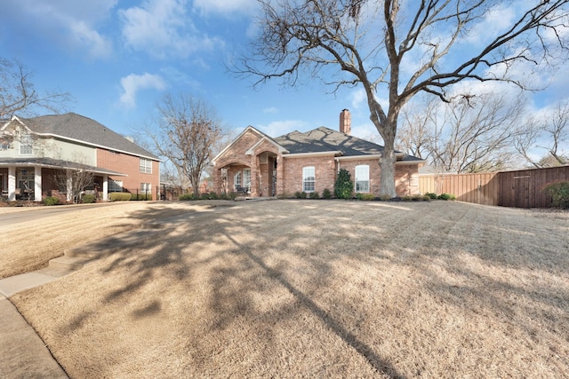 view of front of house with brick siding, a chimney, and fence