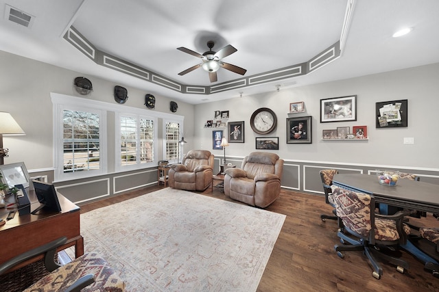 interior space featuring visible vents, a raised ceiling, a ceiling fan, dark wood-style floors, and a decorative wall