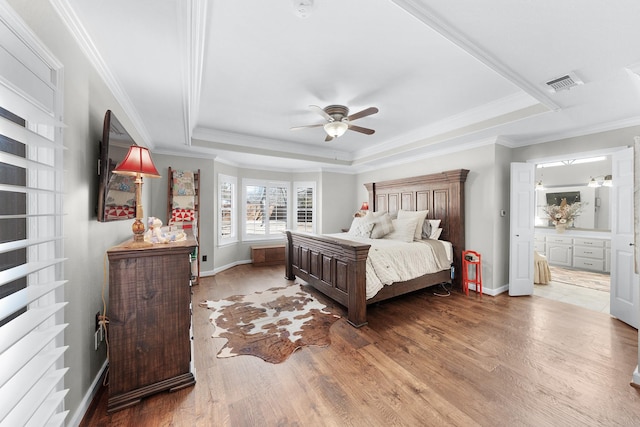 bedroom featuring crown molding, visible vents, a tray ceiling, and wood finished floors