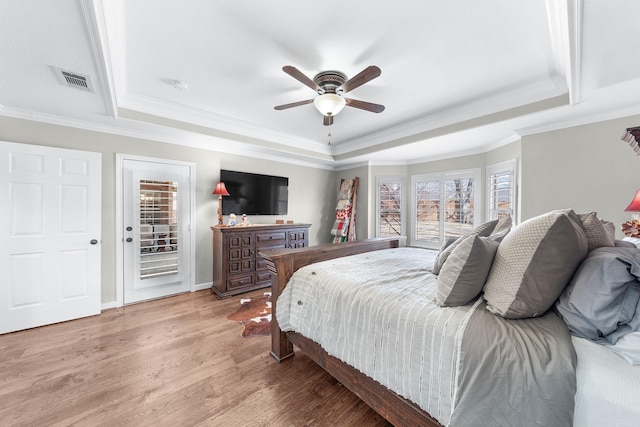 bedroom featuring light wood-type flooring, multiple windows, and a tray ceiling