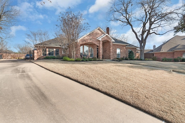 ranch-style house with a chimney, fence, and brick siding