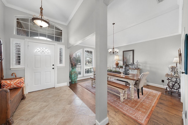 entrance foyer with light wood finished floors, baseboards, an inviting chandelier, crown molding, and high vaulted ceiling