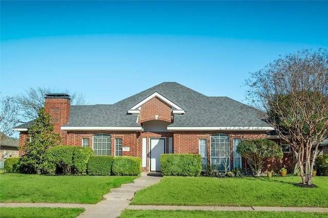 view of front facade with brick siding, roof with shingles, a chimney, and a front yard