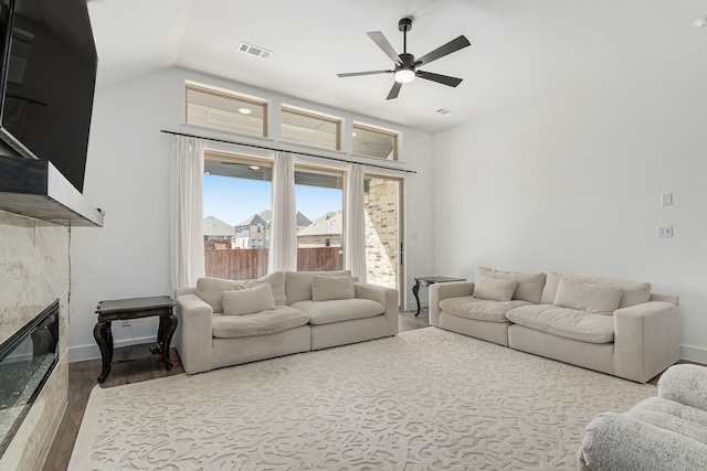 living area featuring visible vents, a ceiling fan, a tile fireplace, wood finished floors, and vaulted ceiling