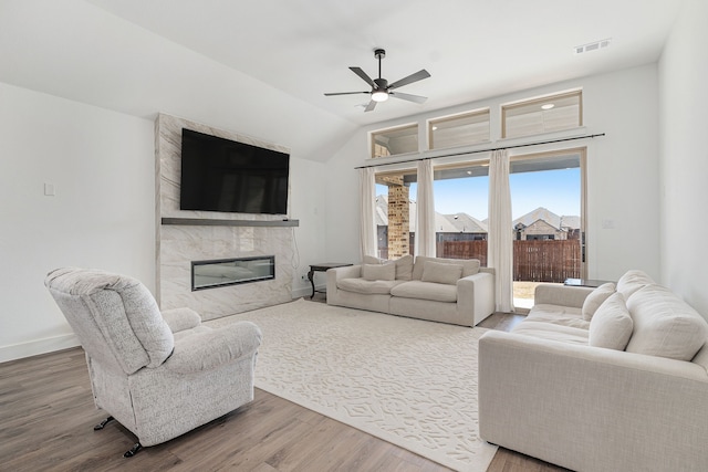 living room featuring lofted ceiling, visible vents, a high end fireplace, wood finished floors, and baseboards