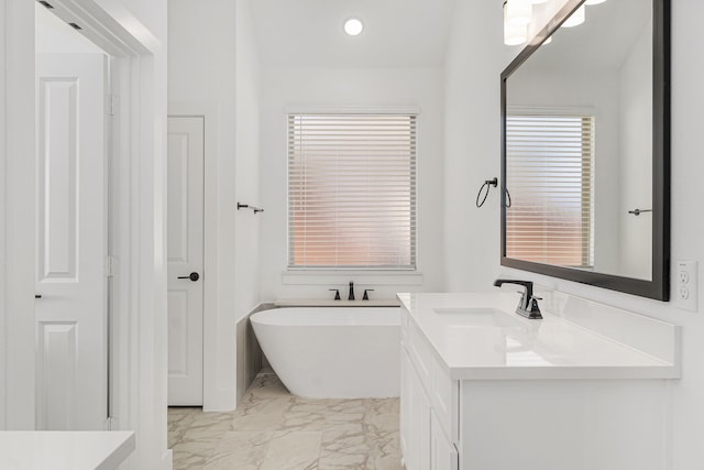 bathroom with marble finish floor, a freestanding tub, and vanity