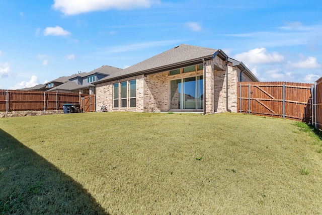 rear view of house with brick siding, a lawn, a shingled roof, and a fenced backyard