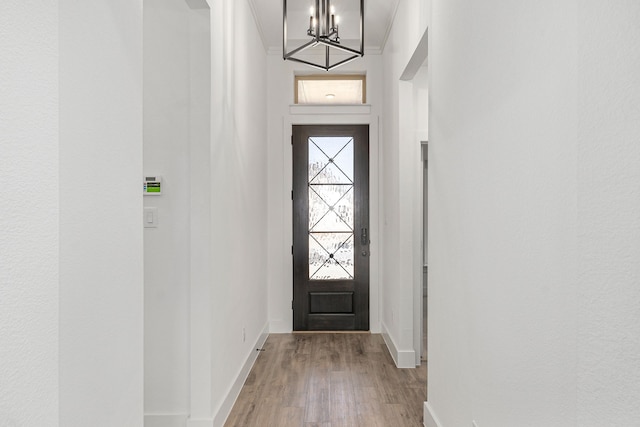 doorway featuring ornamental molding, a chandelier, baseboards, and wood finished floors