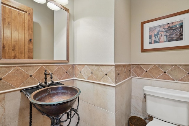 half bathroom featuring tile walls, toilet, a wainscoted wall, and a sink