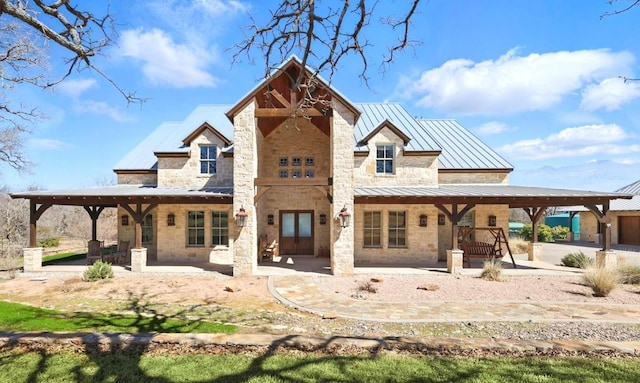 rear view of house with metal roof, stone siding, a patio area, and a standing seam roof