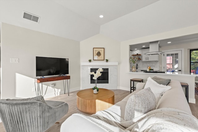 living room featuring lofted ceiling, a premium fireplace, wood finished floors, visible vents, and baseboards