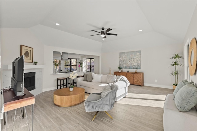 living area featuring vaulted ceiling, wood finished floors, a tile fireplace, and a ceiling fan