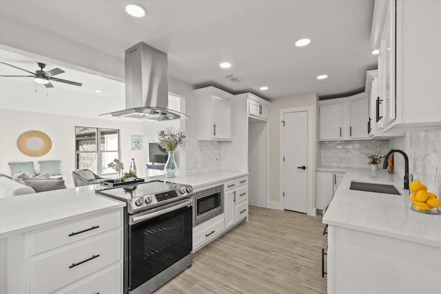 kitchen featuring appliances with stainless steel finishes, open floor plan, island exhaust hood, light wood-type flooring, and a sink