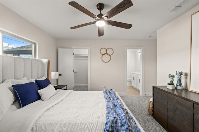 carpeted bedroom featuring a walk in closet, visible vents, ensuite bathroom, a ceiling fan, and baseboards