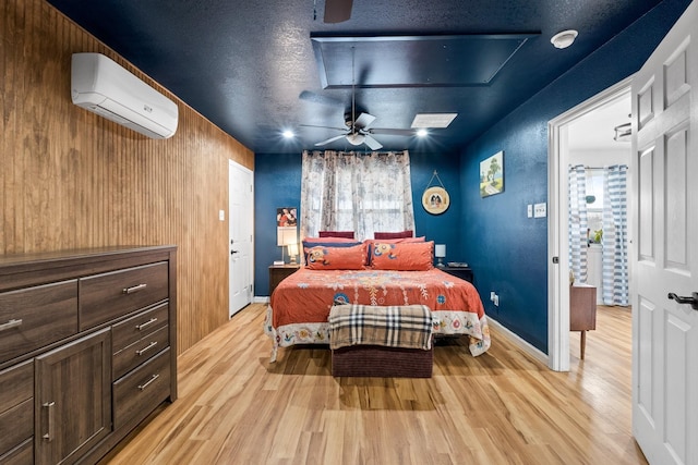 bedroom featuring light wood-style floors, baseboards, a wall mounted air conditioner, and a textured ceiling