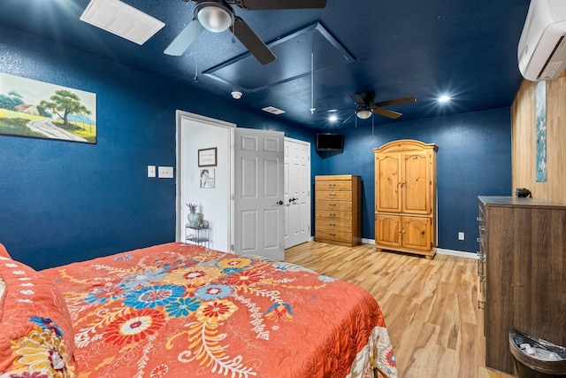 bedroom with baseboards, light wood finished floors, a wall mounted AC, attic access, and ceiling fan